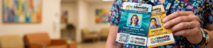 Close-up of a person holding two abc Identity Solutions badges, featuring Sarah Jenkins, RN, healthcare specialist, and David Lee, warehouse lead, against a blurred lobby background. custom ID badges
