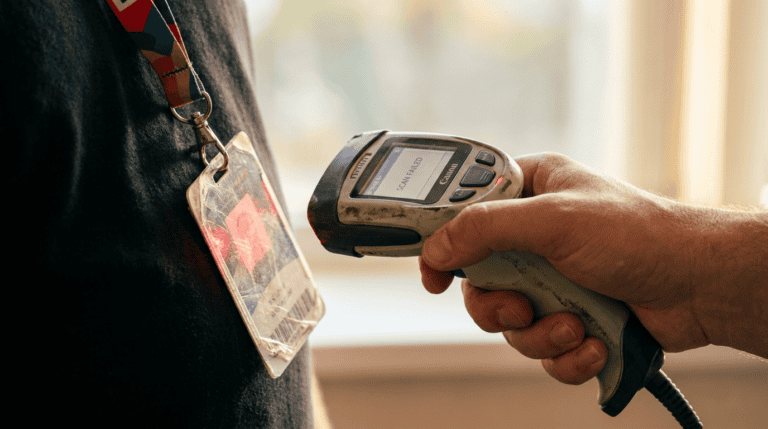 Close-up of a hand-held barcode scanner scanning a worker's ID badge on a lanyard.